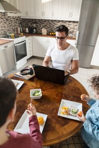 High angle view of siblings eating orange fruit while father working by table at home