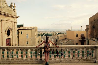 Rear view of woman standing by railing looking at city against sky