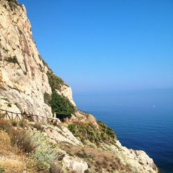 Scenic view of rocky mountain by sea against clear blue sky
