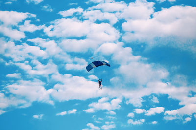 Low angle view of people paragliding against sky