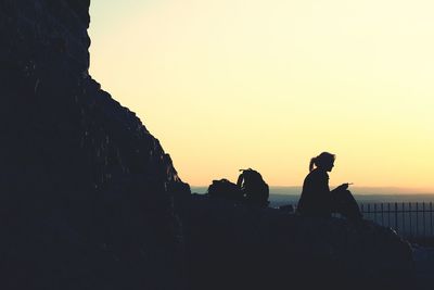 Silhouette woman sitting on rock formation against sky during sunset