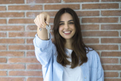 Portrait of young woman standing against brick wall