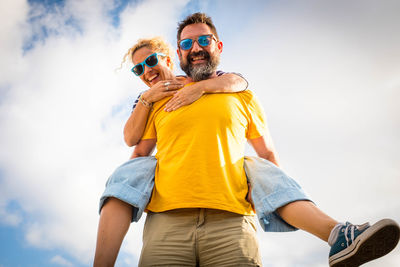 Low angle view of man wearing sunglasses carrying woman on back against sky
