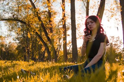 Young woman using smart phone while sitting on grassy land
