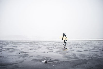 Surfer walking along the beach in maine during a winter snow storm