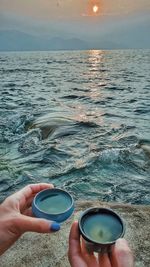 Hands hold a bowl of tea on the shore