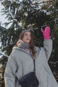 Woman with freckles in winter clothes with mittens outdoors enjoys winter, smiles