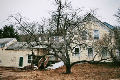 Bare trees by old building against sky