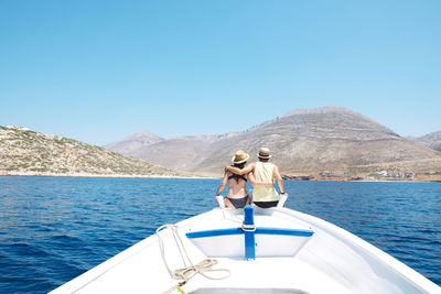 Greece, back view of couple sitting arm in arm on bow of a boat looking at amorgos island