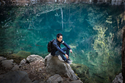 Full length of backpacker sitting on rocks by lake