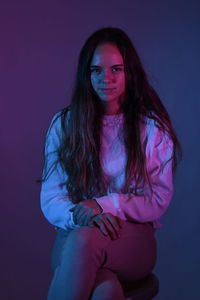 Portrait of teenage girl sitting over purple background