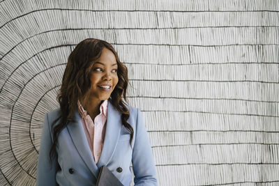 Smiling businesswoman looking away while standing against wall