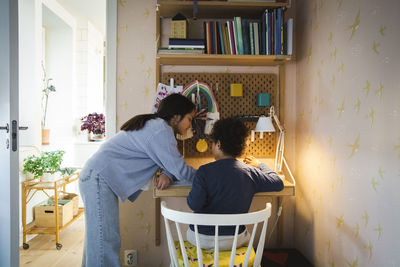 Side view of sister helping brother while studying at home