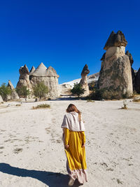 Rear view of woman walking on desert against clear sky during sunny day