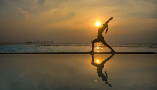 Reflection of woman in swimming pool against sky during sunset