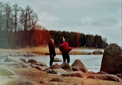 Male friends standing at shore against sky