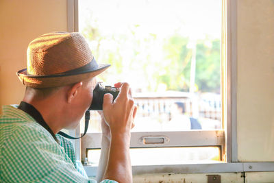 Portrait of man holding hat against window