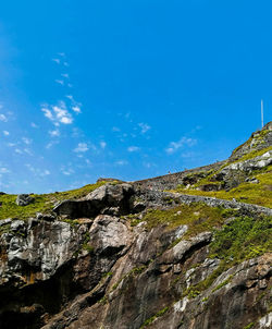 Low angle view of rocks on mountain against blue sky