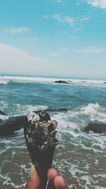 Close-up of hand holding sea against sky