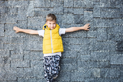 Portrait of boy with arms outstretched standing against stone wall