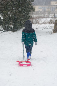 Rear view of girl with sled on snow