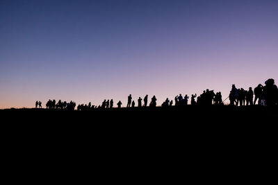 Silhouette people on field against clear sky during sunset
