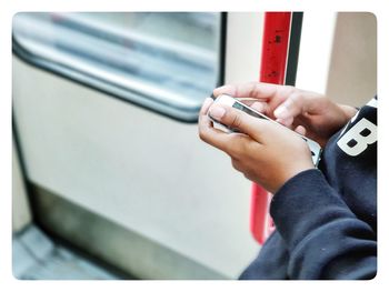 Midsection of person using phone in train