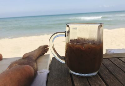 Low section of man with iced coffee against sea