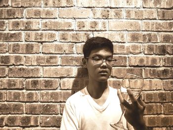 Young man holding wineglass against brick wall