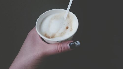 Close-up of hand holding coffee cup against black background