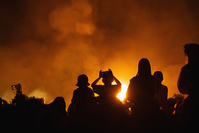 Backlit silhouetted crowd enjoying festival at night.