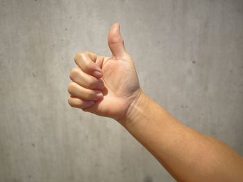 Close-up of hand gesturing thumbs up against wall