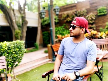 Young man looking away while standing against plants