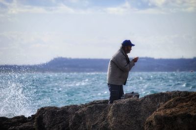 Man standing on rock looking at sea against sky