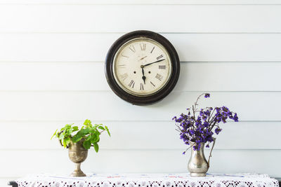 Flower vase on table with clock mounted on wall at home