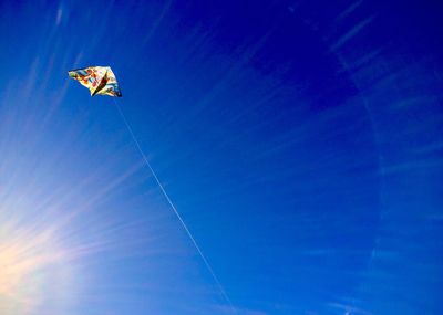 Low angle view of kite flying against blue sky on sunny day