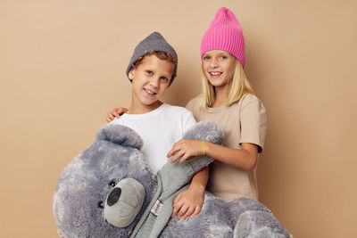 Portrait of sibling holding stuffed toy against beige background