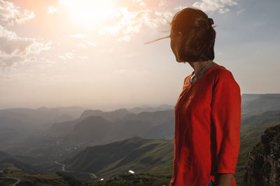 A romantic girl standing on a mountain and admiring the sunrise or sunset over the mountain, the