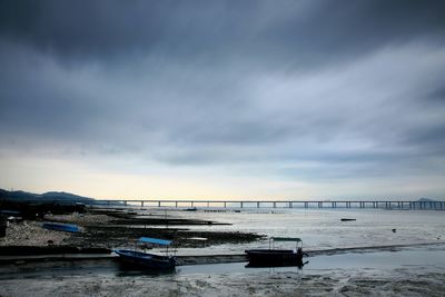 Boats moored at beach against cloudy sky during sunset