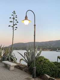 Street light by sea against sky during sunset