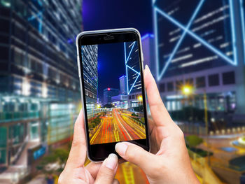 Digital composite image of hand holding mobile phone in city