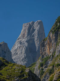 Low angle view of rocky mountains against clear blue sky