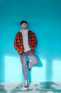 Happy male with beard in casual wear looking at camera while standing near blue wall in light spacious building with windows