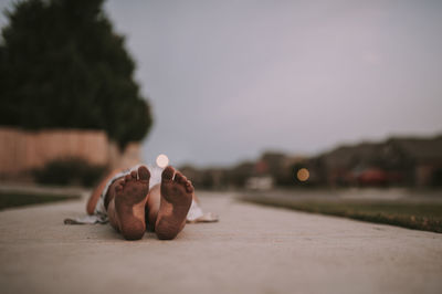 Low section of girl lying on footpath at lawn during dusk