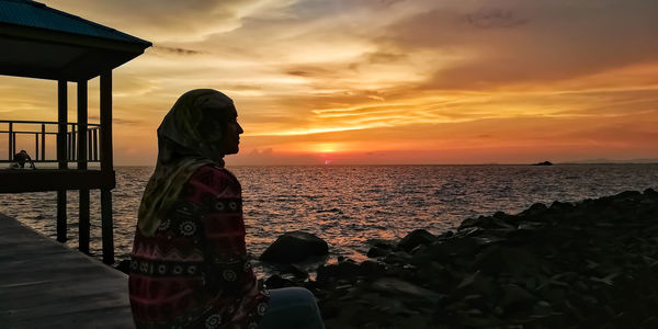 Side view of thoughtful woman sitting at beach during sunset