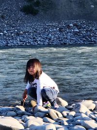 Girl crouching on stones by sea