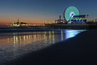 Illuminated ferris wheel by beach at night