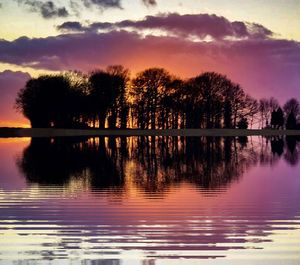 Silhouette trees by lake against sky during sunset