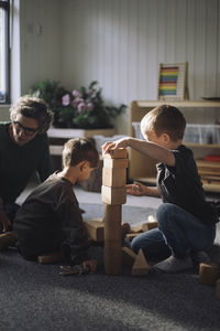 Schoolboys playing with toy blocks with female teacher in classroom at kindergarten