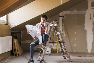 Young woman renovating her new home, holding construction plan